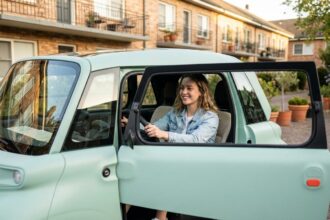 Jeune femme au volant d'une Fiat Topolino sans permis garée en ville, souriante et détendue