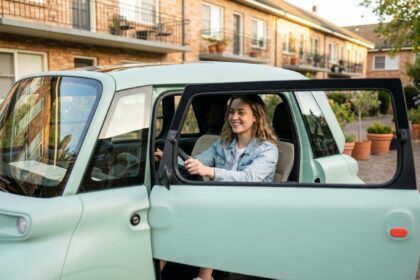 Jeune femme au volant d'une Fiat Topolino sans permis garée en ville, souriante et détendue